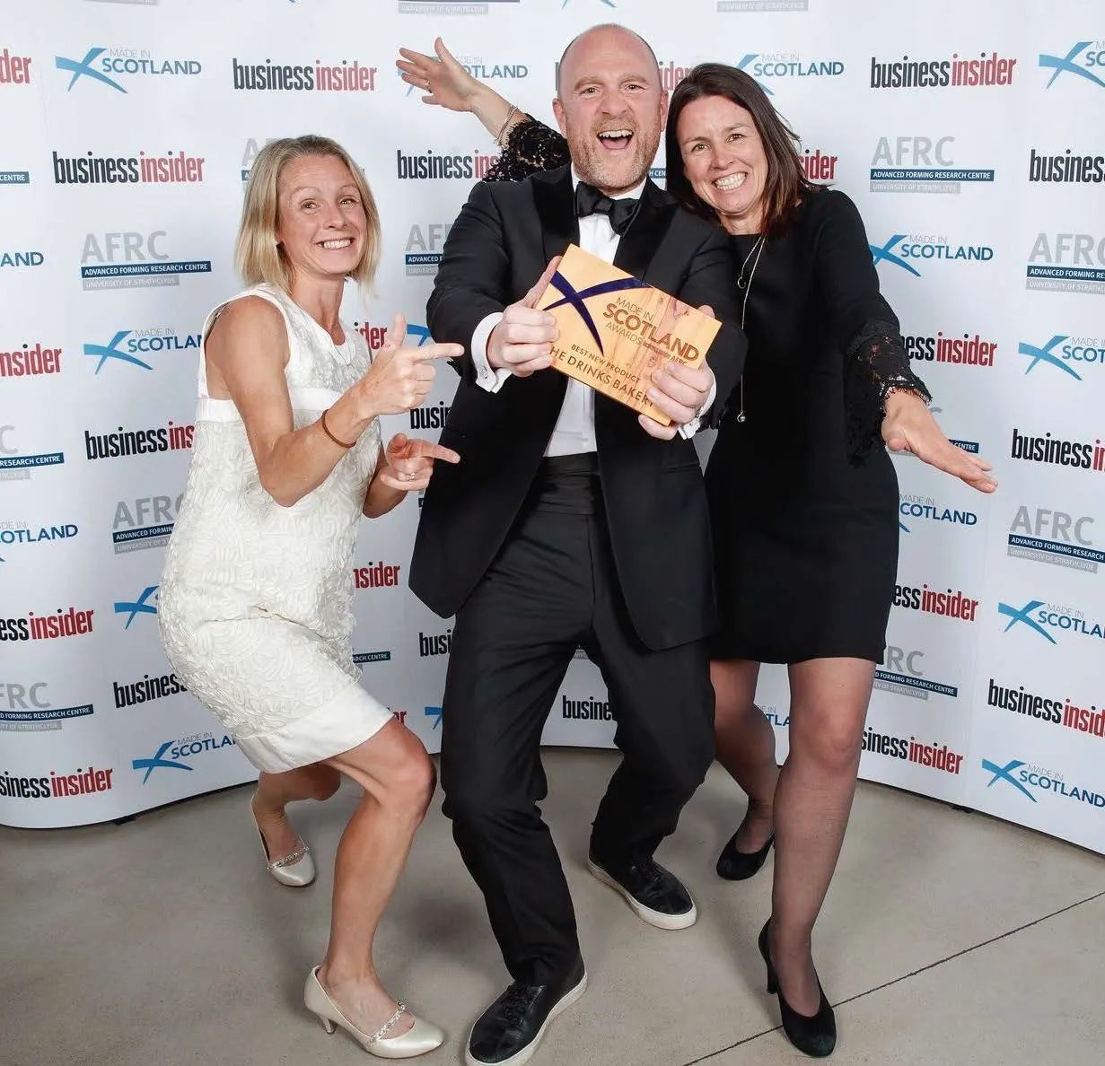 Three people posing together in front of a branded event backdrop. Andy Murray (the central person in a black tuxedo) holds a wooden award plaque that reads 'MADE IN SCOTLAND - Best New Product'.
