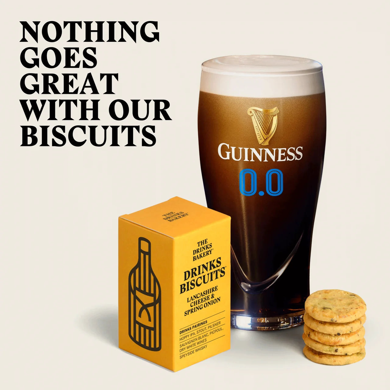 A promotional product shot showing a yellow box of Drinks Biscuits, a pint of dark Guinness 0.0 beer, and a stack of round biscuits on a light beige background, with the text 'NOTHING GOES GREAT WITH OUR BISCUITS' at the top left.
