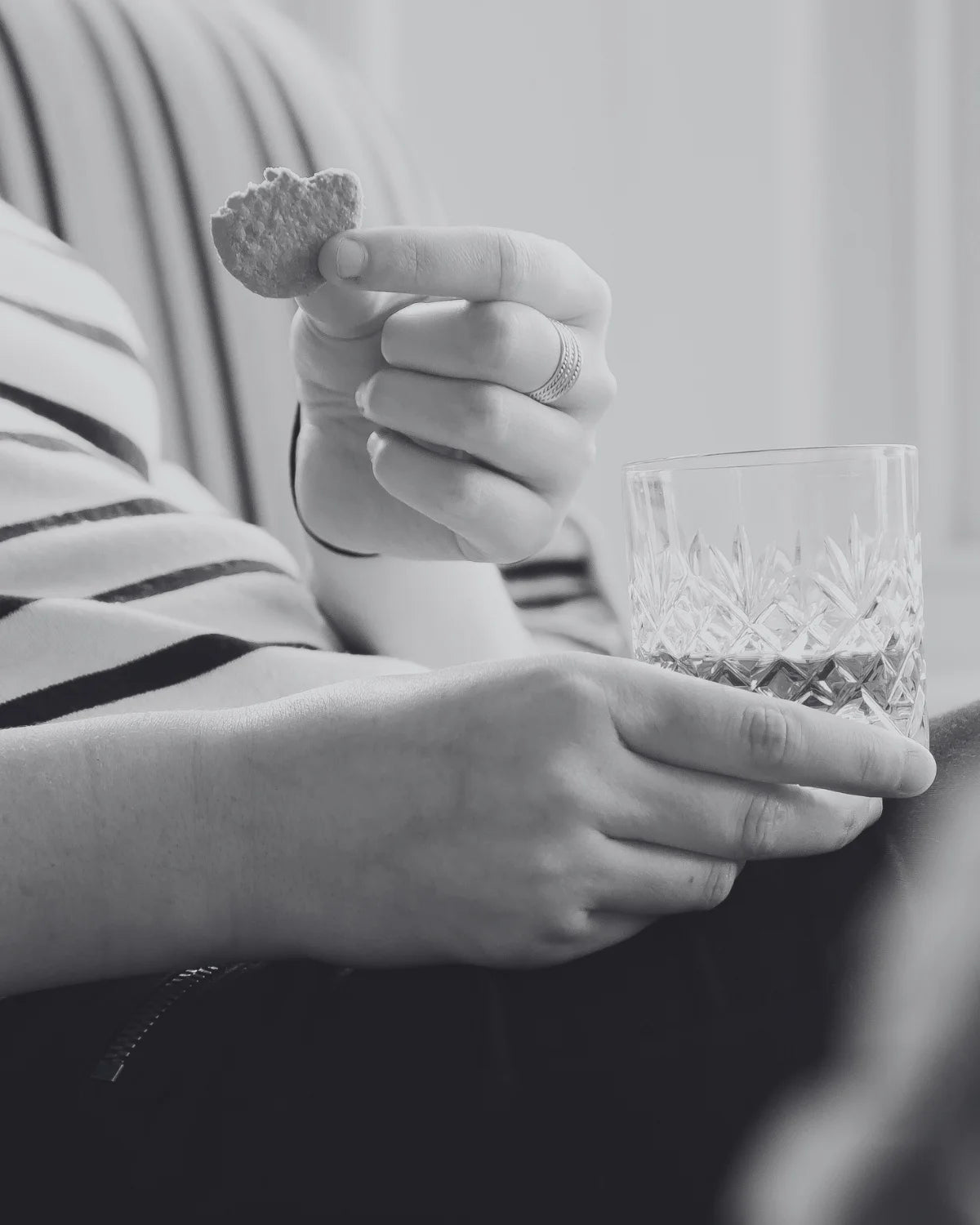 Person holding a crystal glass and a savoury drinks biscuits in a close-up shot.