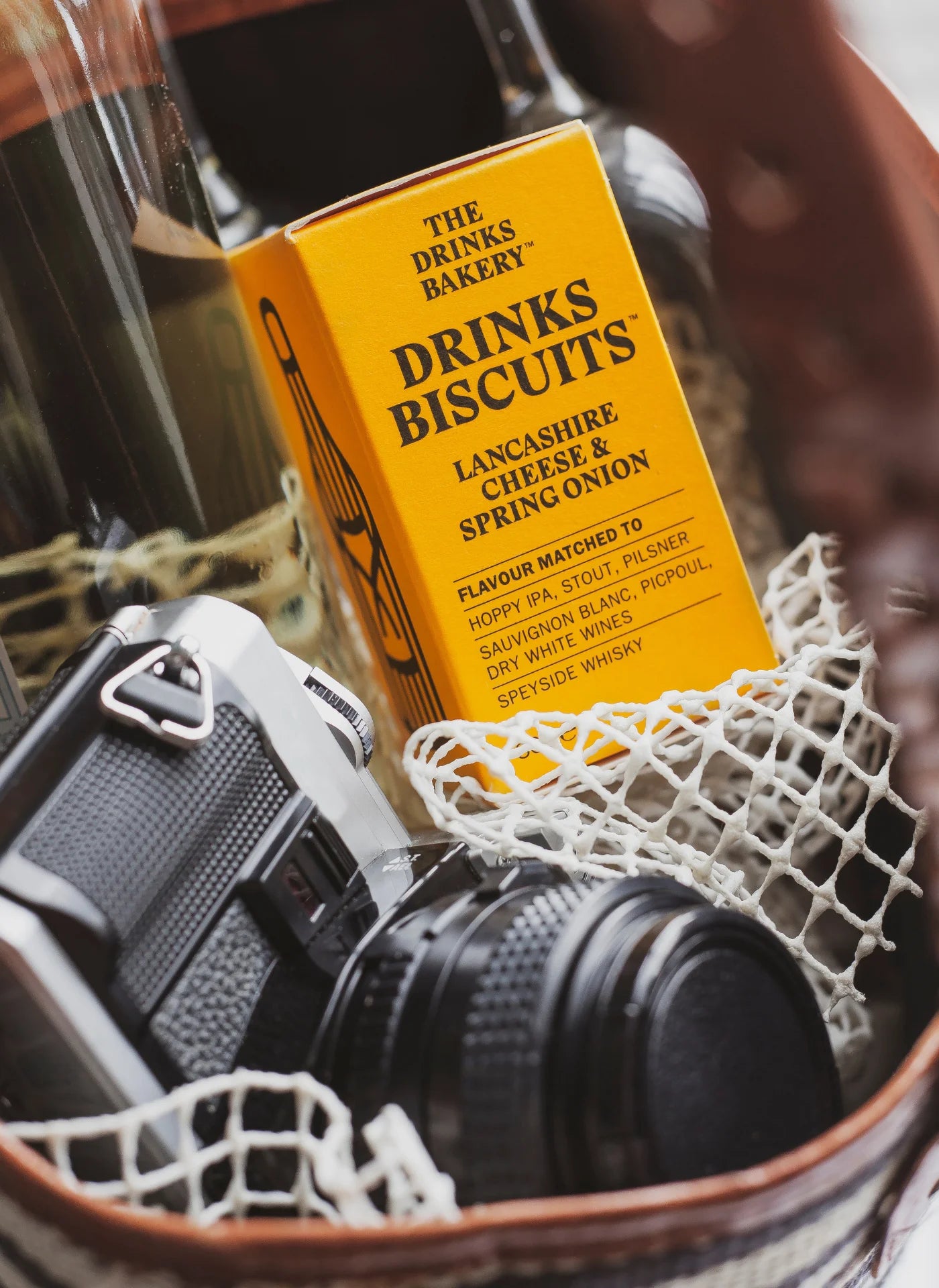 Bottle of white wine, drinks biscuits, and a camera in a bag with a blurred background.