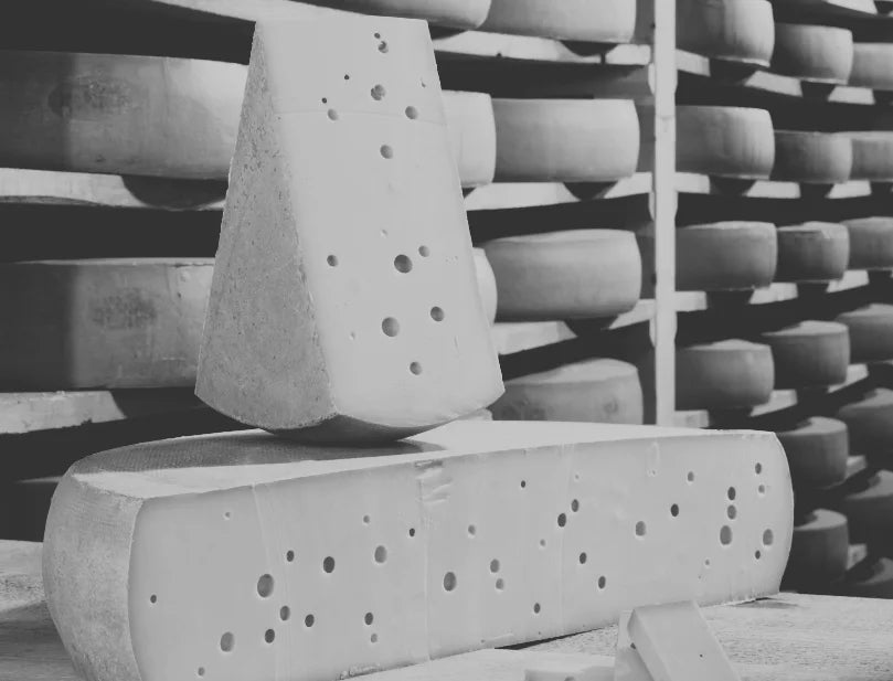 Wall of blocks of cheese on shelves, and a close up of a cut open block of cheese.